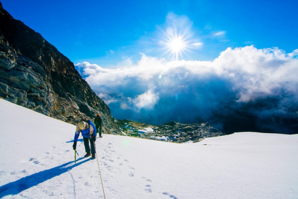 Climbers ascending the snow-capped peaks of Mt. Rwenzori in Uganda, surrounded by dramatic alpine scenery and lush tropical vegetation."